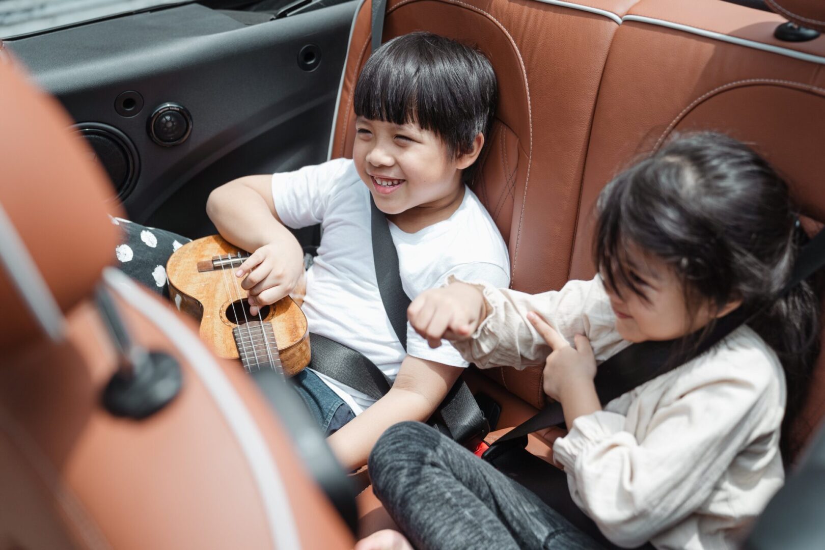 Two children in a car seat playing with a guitar.